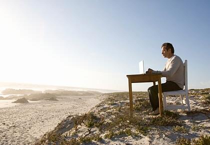 Ein Mann sitzt an einem Schreibtisch, der mitten am Strand steht.