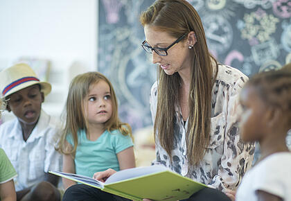 Eine junge Lehrerin liest Kindern aus einem Buch vor.