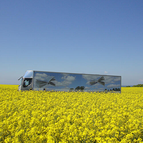 Eine Fahrbücherei der Büchereizentrale Schleswig-Holstein fährt durch ein Rapsfeld.
