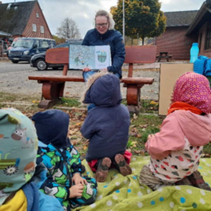 Frau zeigt Kindern ein aufgeklapptes Buch